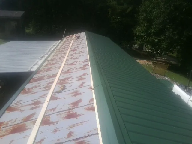 Old rusted panels beside newly installed green metal roofing — Wind Damage Roof Repair by Roofing Brothers in Harvey