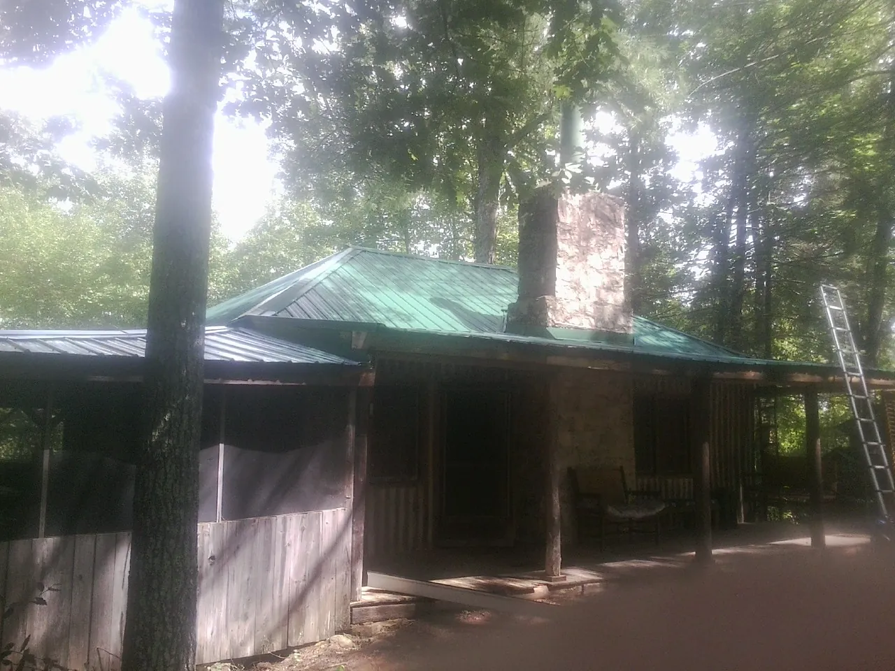 Green metal roof and stone chimney above a log cabin porch in Harvey